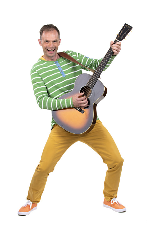 Kirjaviin vaatteisiin pukeutunut mies hymyilee ja soittaa kitaraa. Kuva Jiri Halttunen