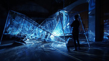 sinisensävyinen valoveistos, jossa kristallimaista valoa, oikealla seisoo ihminen. Kuva Théoriz